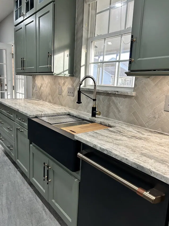 Kitchen with sage green cabinets, herringbone stone backsplash, and farmhouse sink by CNB Renovations